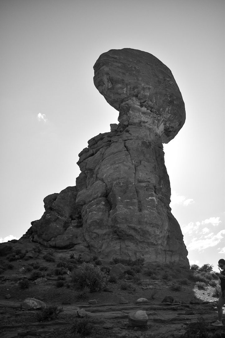 Large, mushroom-shaped rock formation in a desert landscape, silhouetted against the sun.