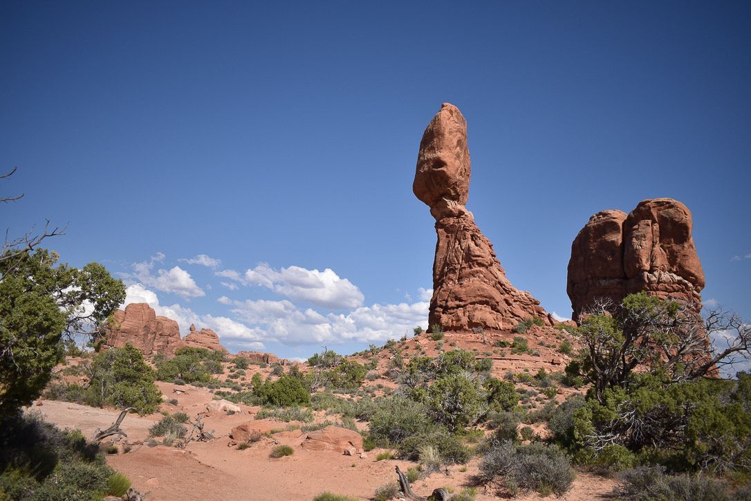 Balanced Rock, Arches National Park, Utah. Towering sandstone formation against a blue sky, desert vegetation in foreground.