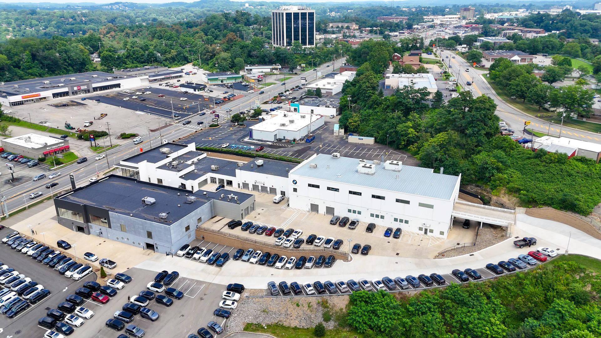 Aerial view of a commercial area with various buildings, parking lots, and a tall office building in the background.