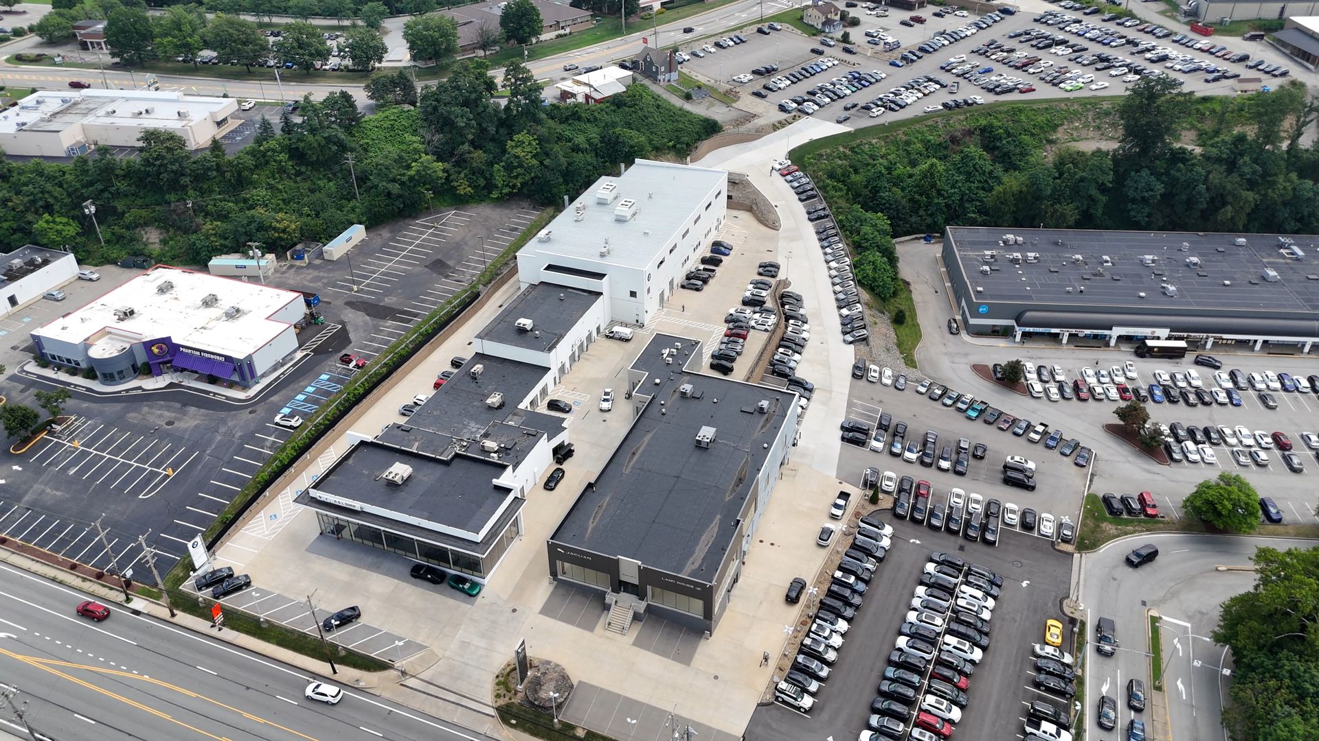 Aerial view of a car dealership with rows of vehicles and buildings in a suburban area.