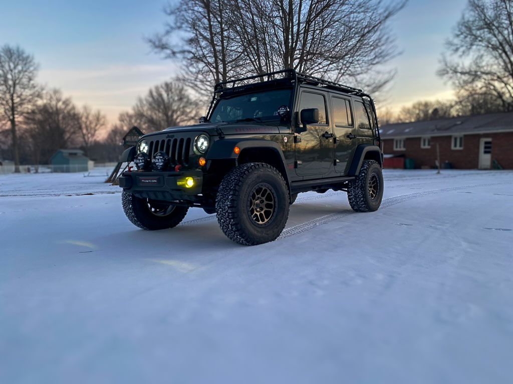 Dark green Jeep with black roof rack parked in snow.