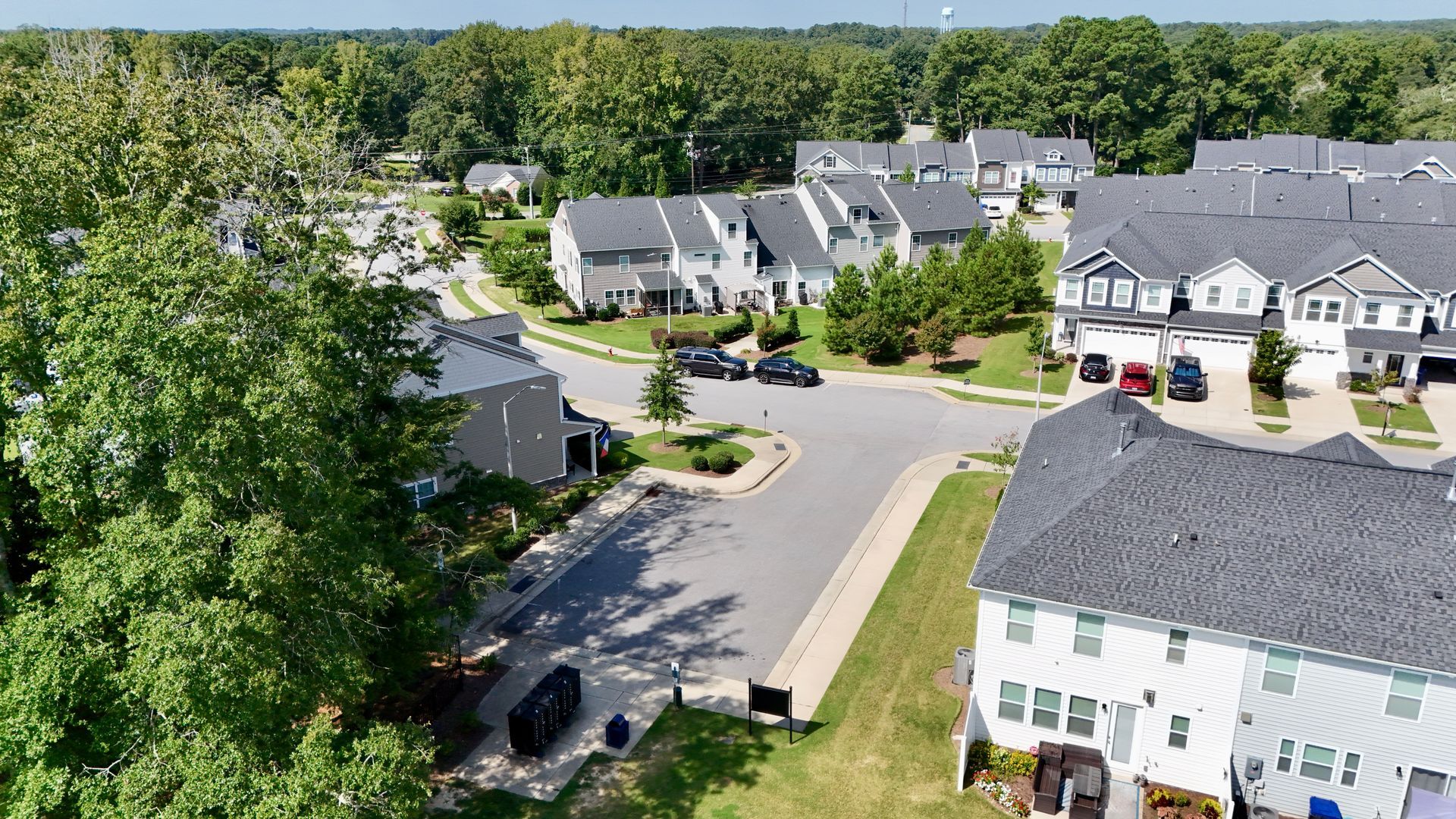 Aerial view of a suburban neighborhood with houses, trees, and a street on a sunny day.