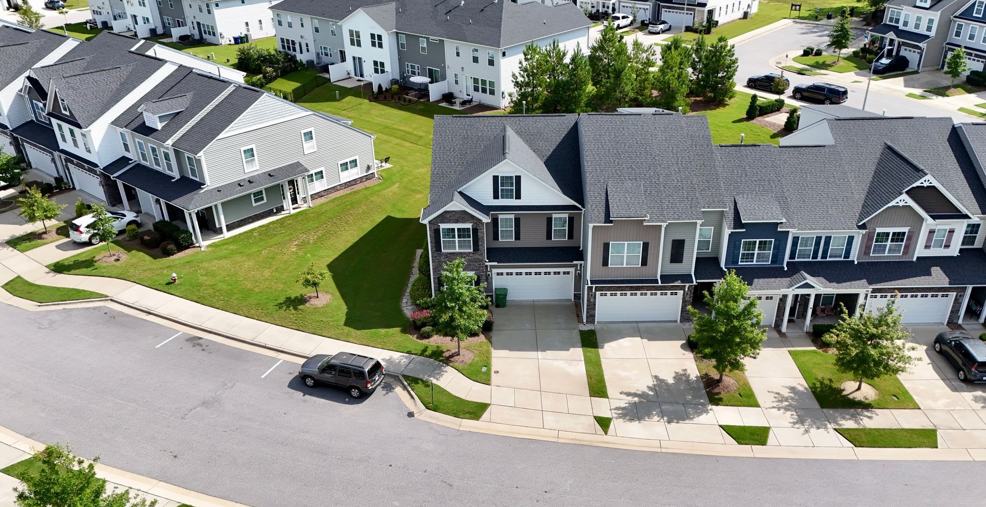Row of townhouses in a residential neighborhood with driveways, lawns, and a black SUV parked on the street.