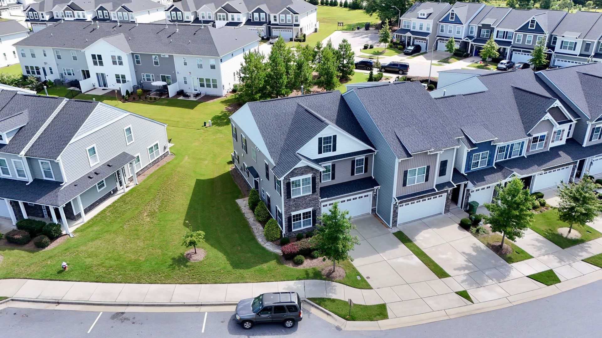 Aerial view of suburban homes with various siding colors, green lawns, and a car parked on the street.