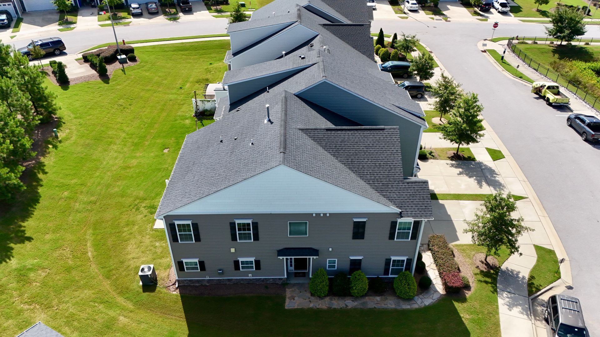 Aerial view of multi-unit gray townhouses with dark gray roofs and green lawns.