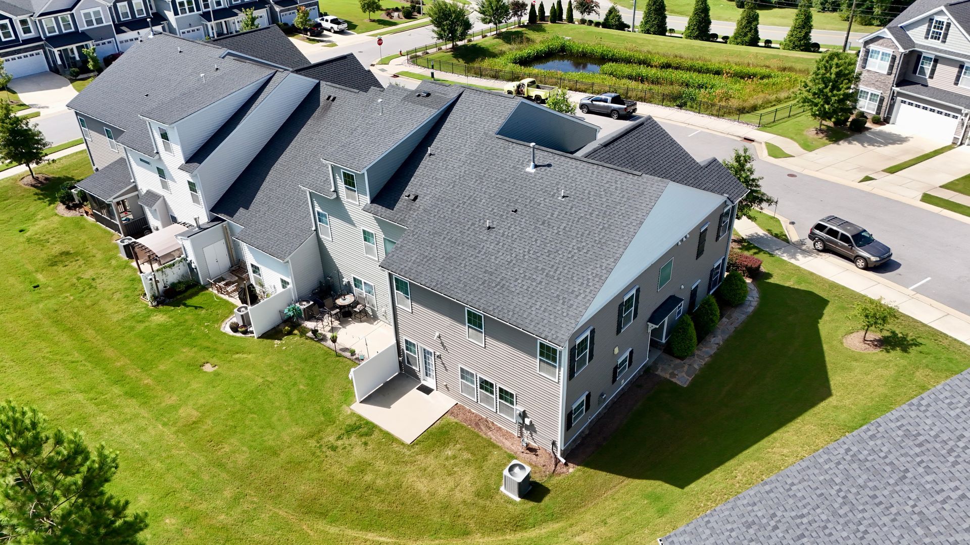 Aerial view of townhouses with gray roofs, green lawns, and a car driving on the street.