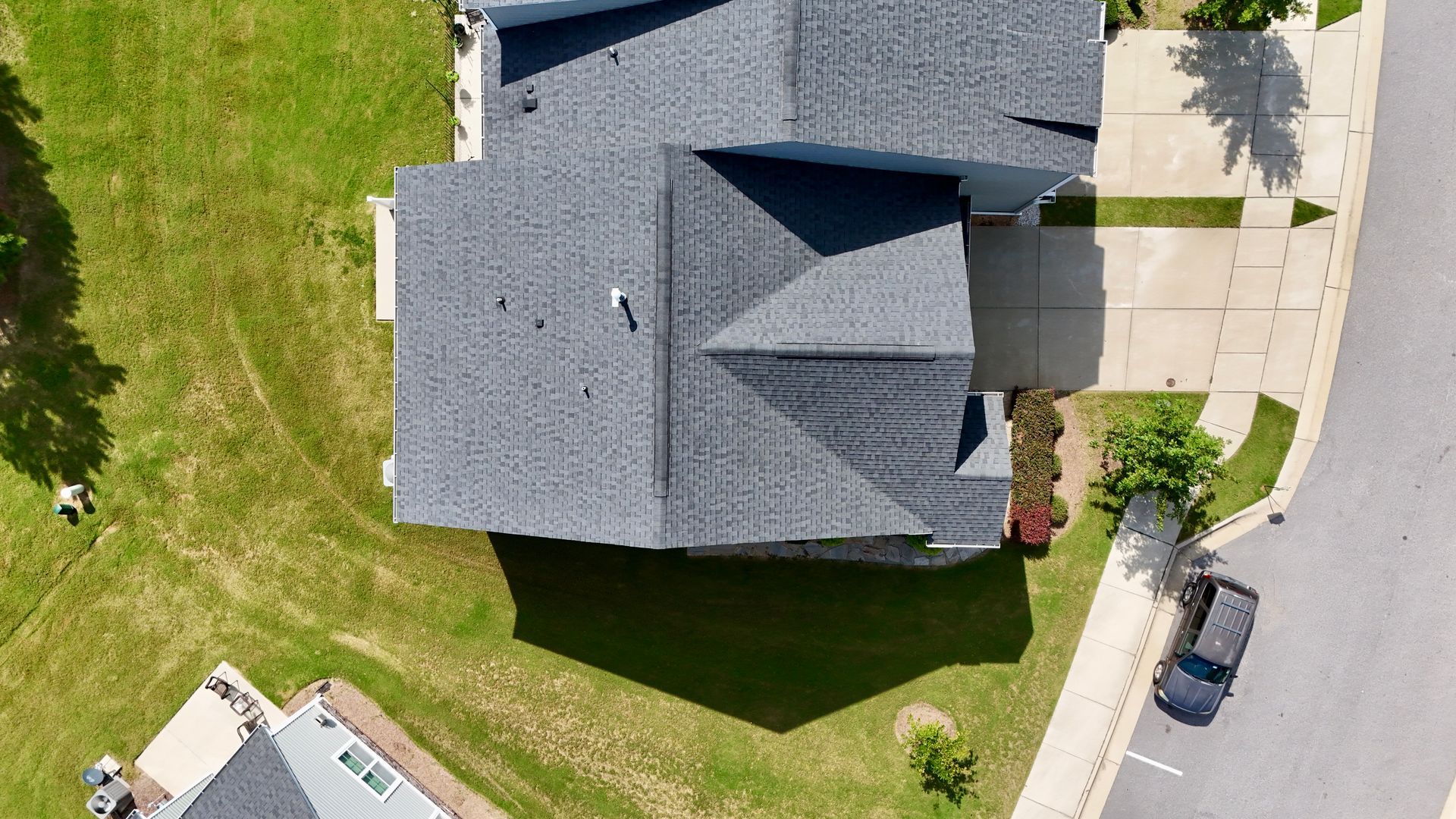 Overhead view of a gray-roofed house with a driveway, surrounded by green grass and a road.