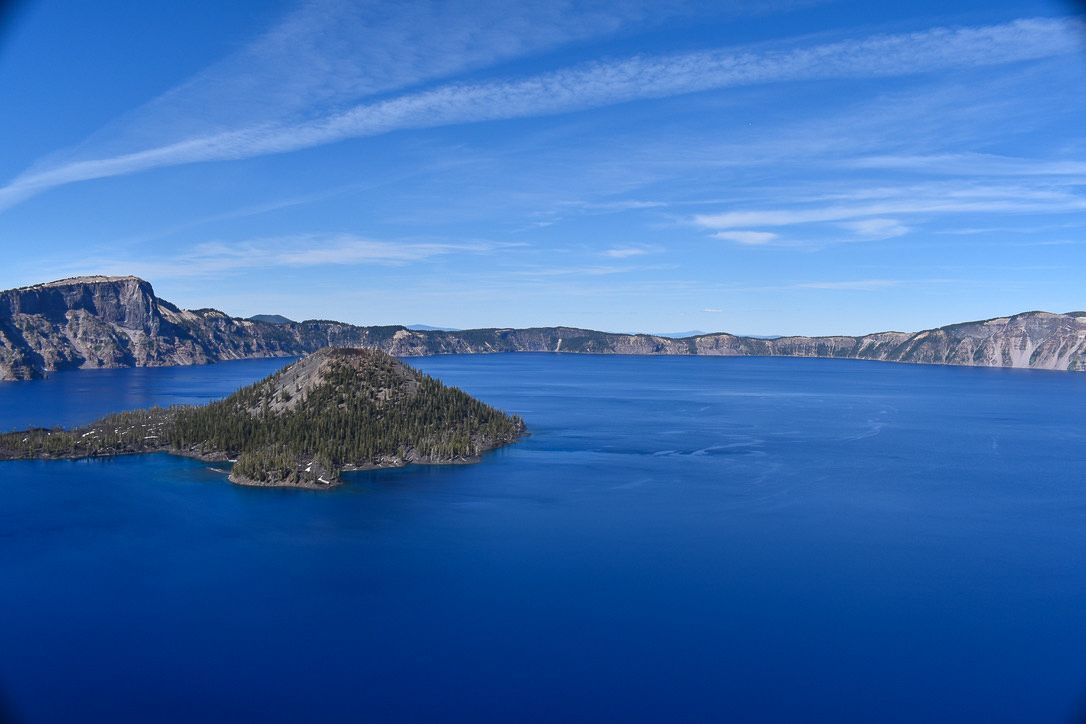 Crater Lake with Wizard Island under a bright blue sky. Mountains surround the deep blue water.