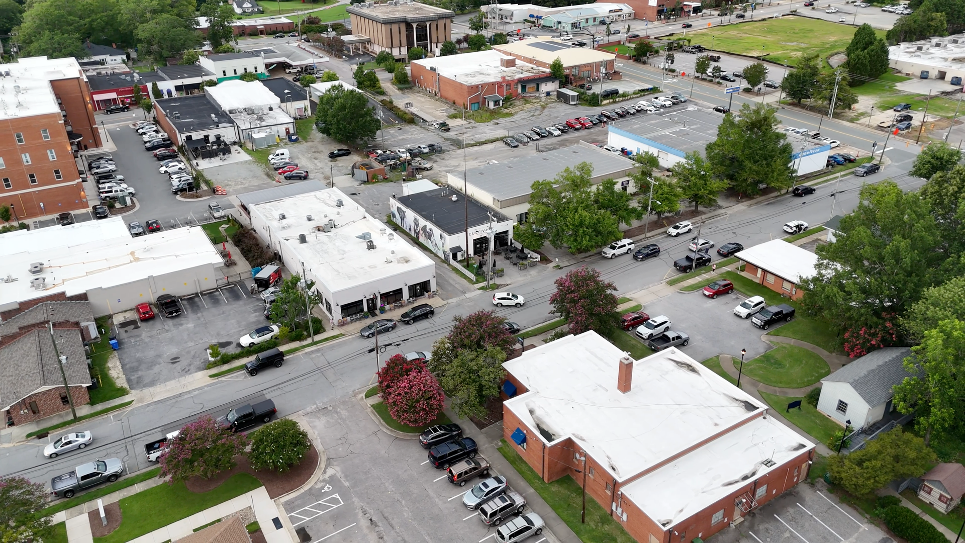 Aerial view of a small town intersection with buildings, cars, and trees.