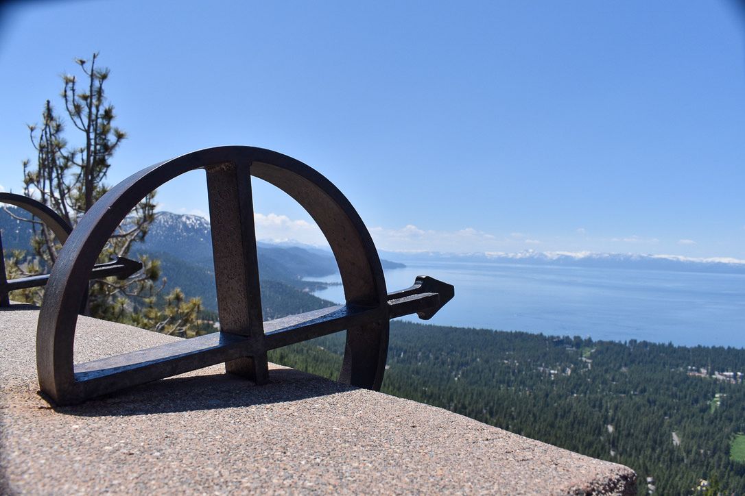 Anchor sculpture overlooks Lake Tahoe and forested shoreline on a sunny day.