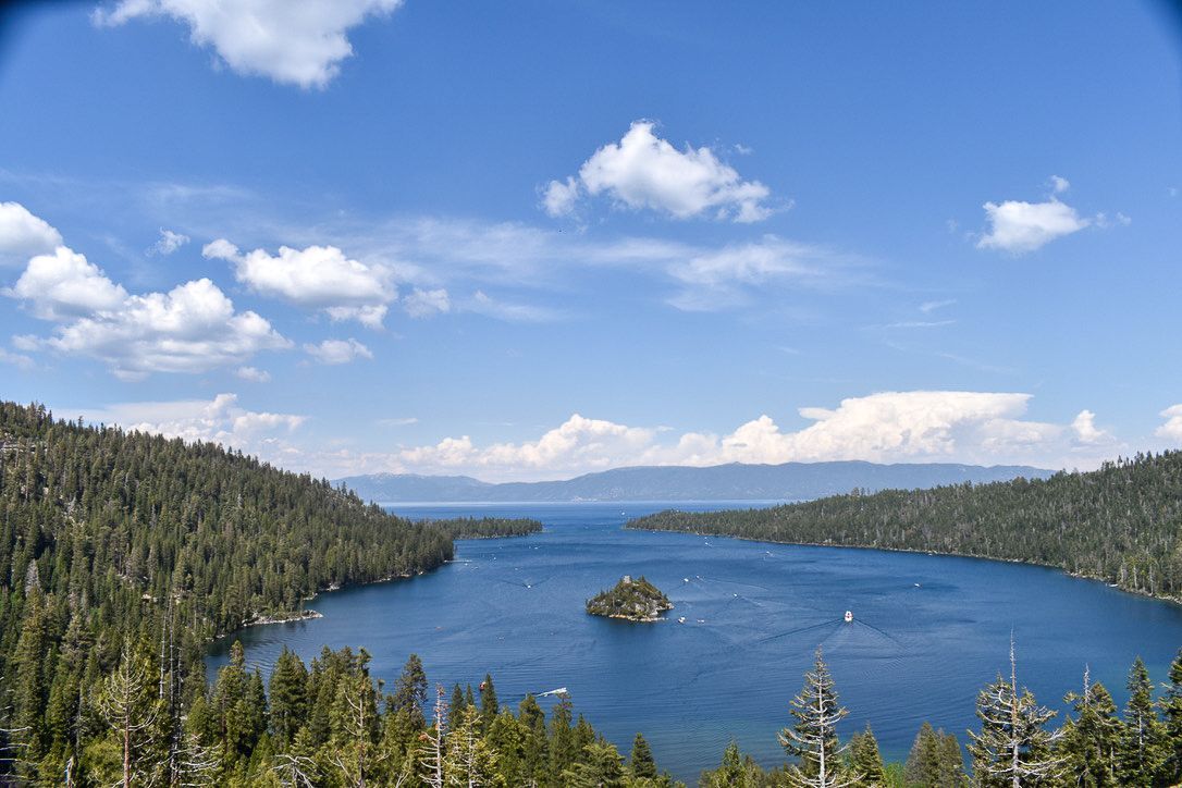 Blue lake surrounded by green trees under a bright blue sky with fluffy white clouds.