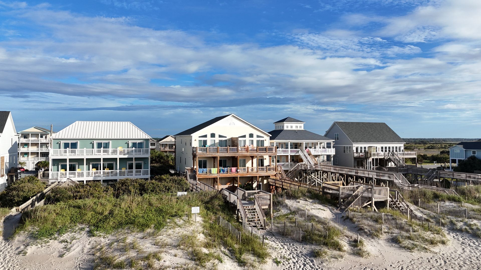 Beach houses on a sandy shore under a partly cloudy blue sky.