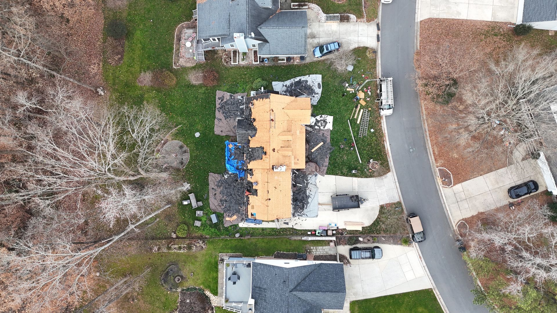 Aerial view of a house with damaged roof, construction debris, and surrounding neighborhood.