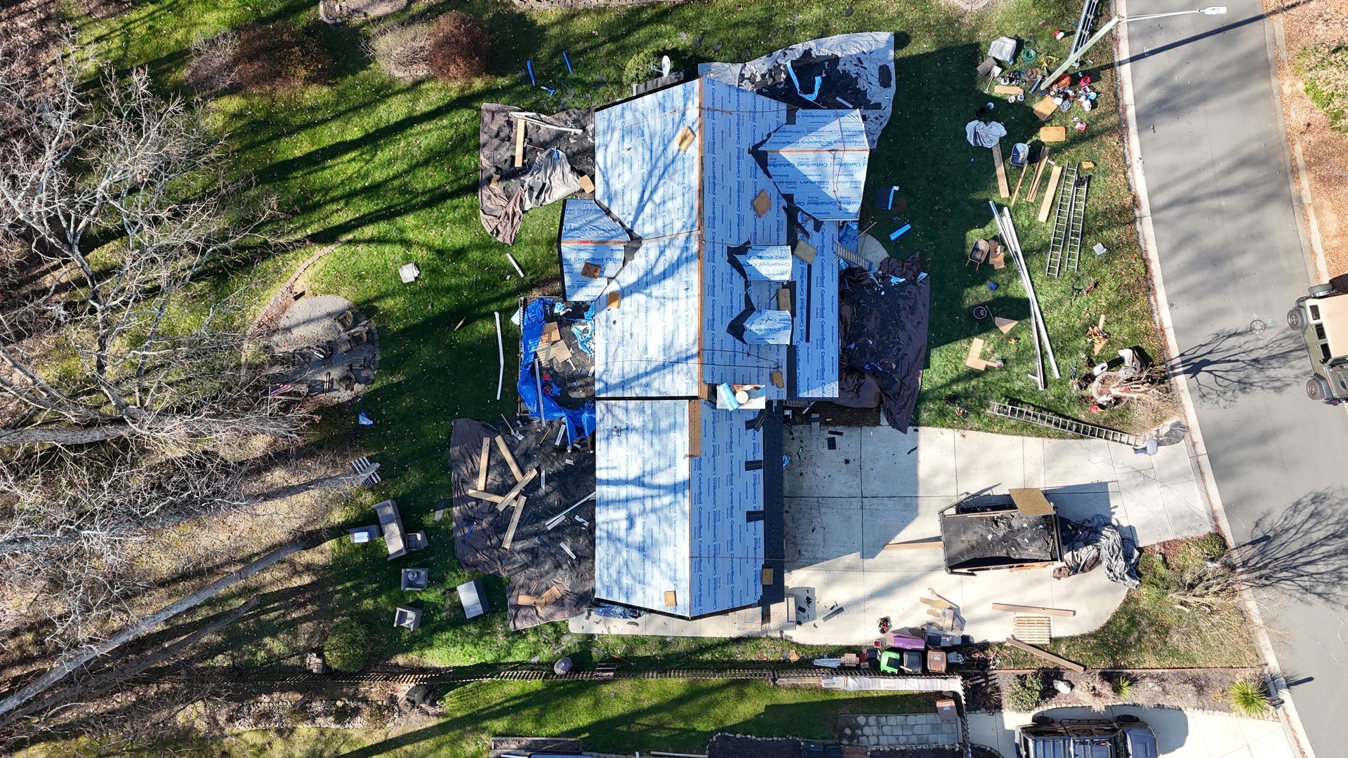 Aerial view of a house with roofing materials and equipment, near a road.