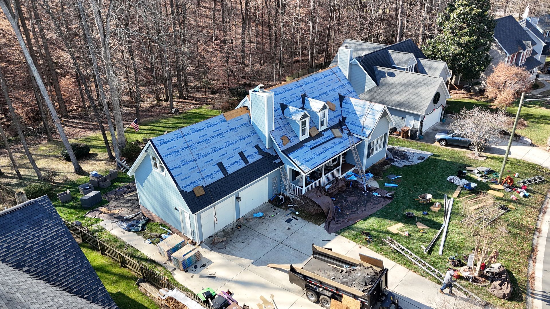 House under construction, partly covered in blue tarp, with a dumpster in the driveway.