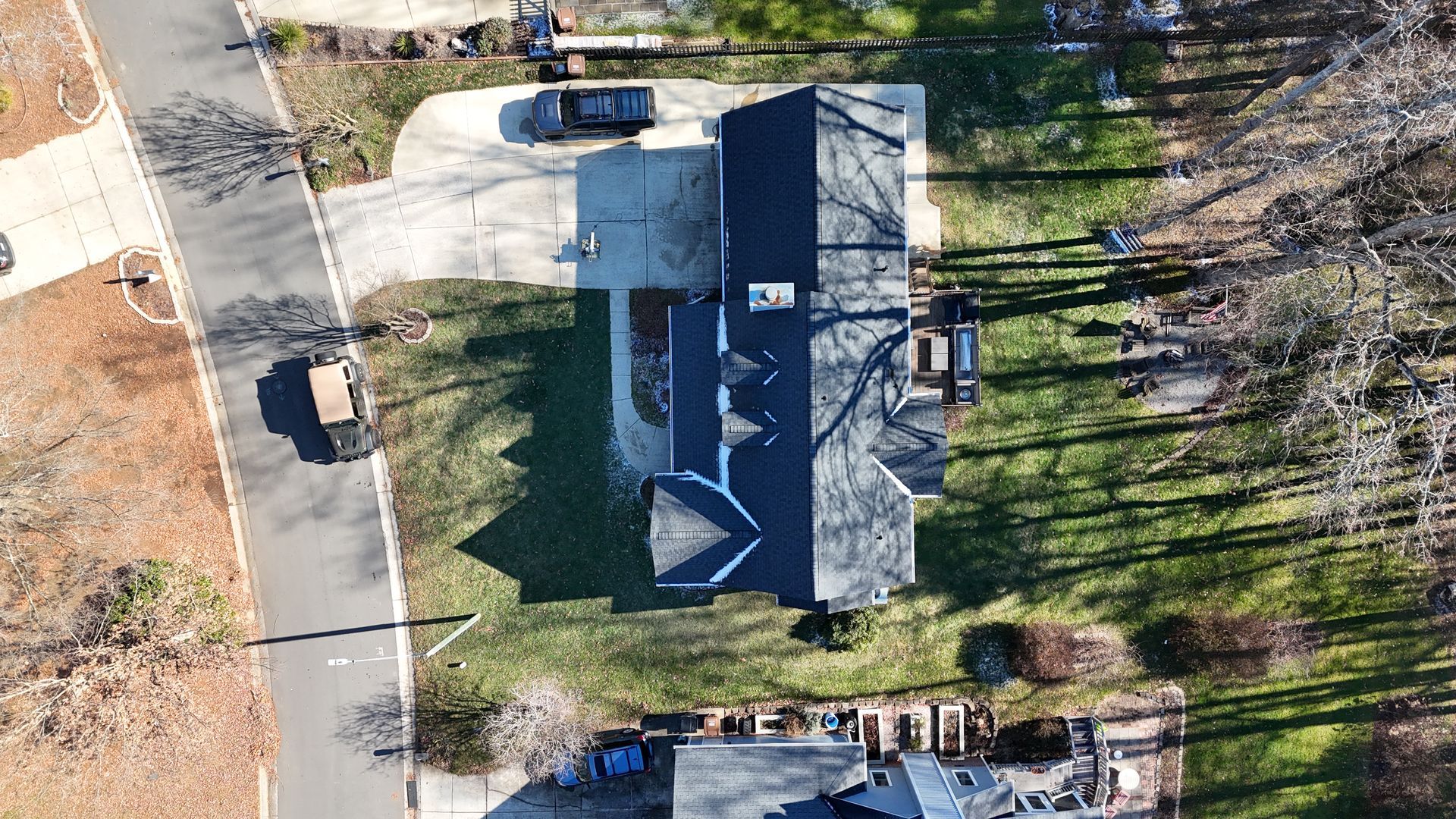 Aerial view of a house with a dark roof, driveway, and surrounding greenery.