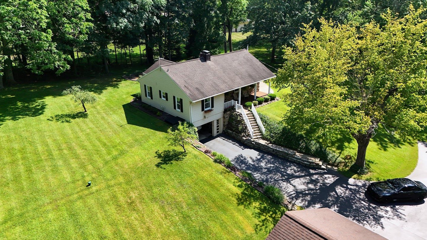 Aerial view of a house with a green lawn, driveway, and trees.