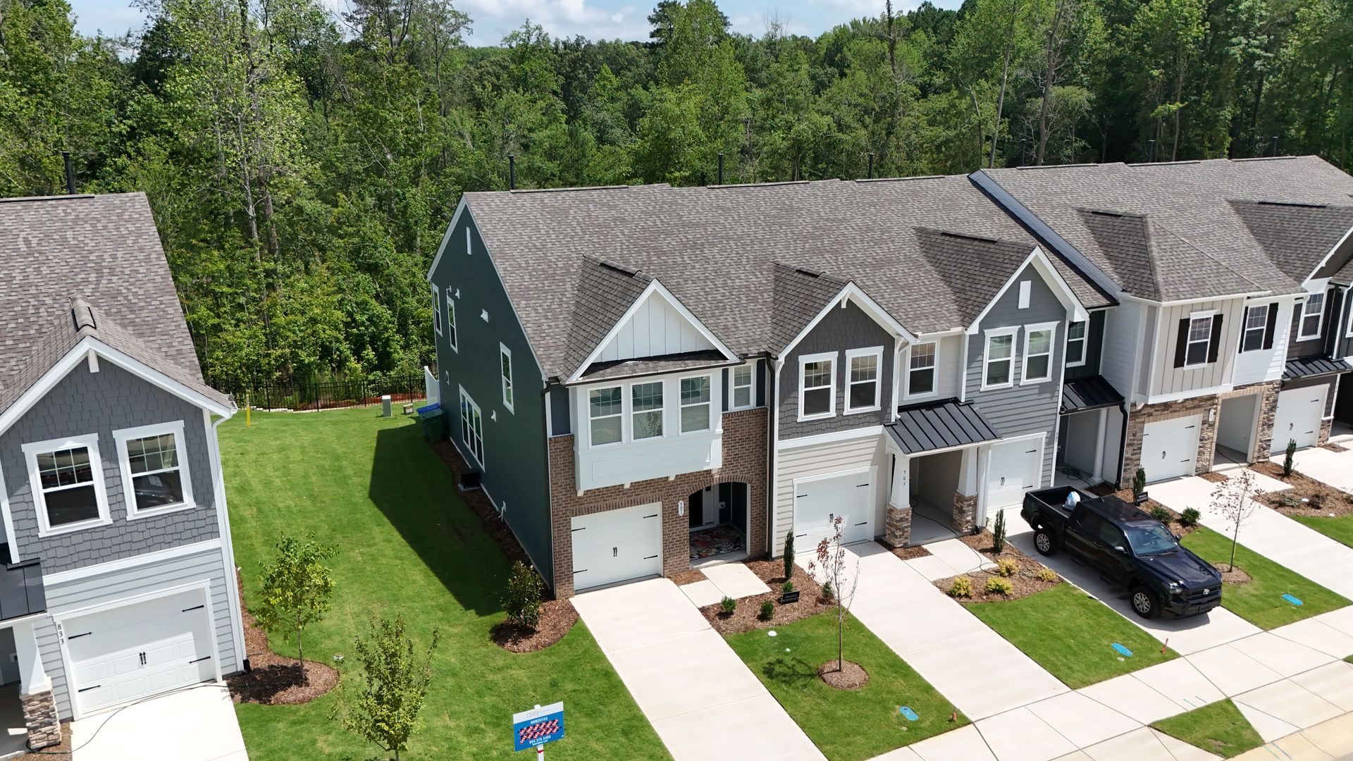 Row of new townhomes with gray siding and attached garages. Green lawns and trees in the background.