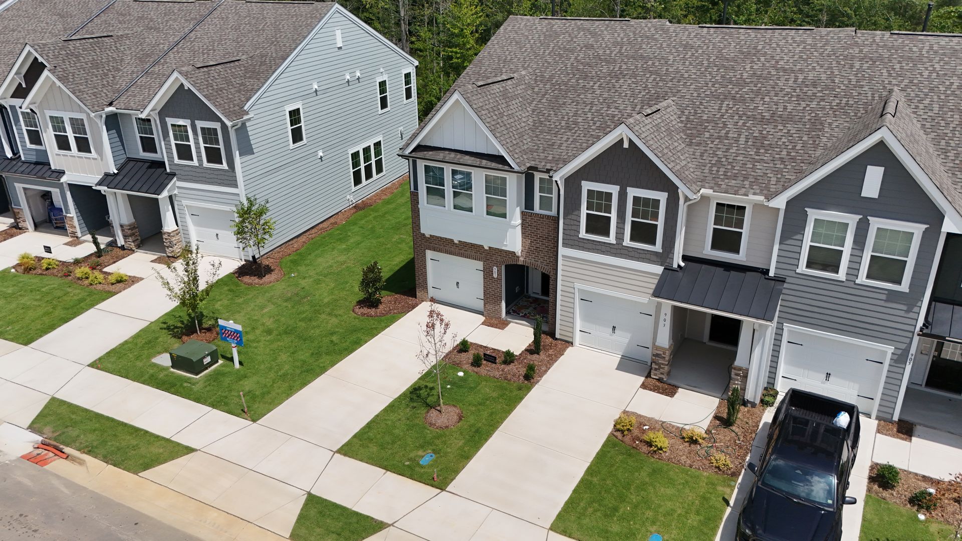 Row of modern townhomes with gray and white exteriors, driveways, and green lawns.