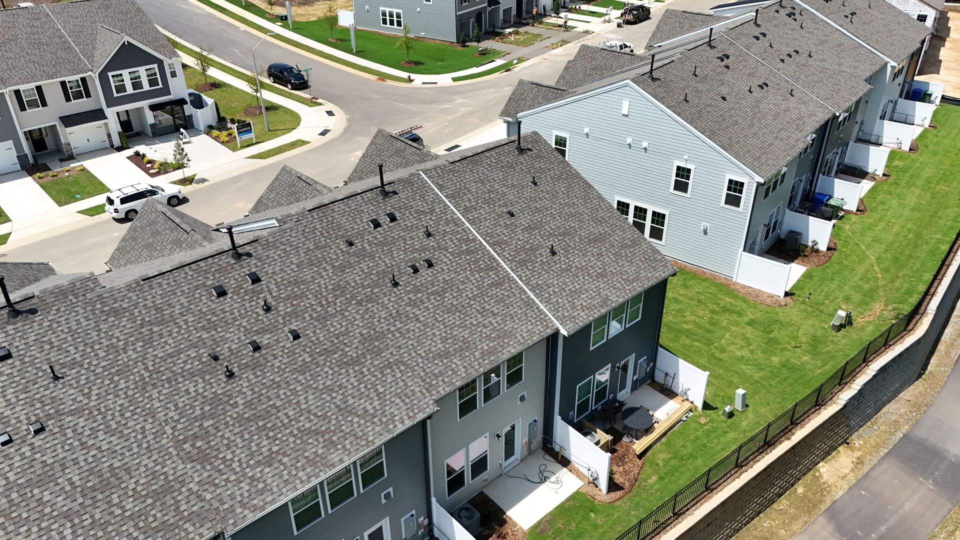 Aerial view of townhouses with gray roofs and siding, green lawns, and a road.