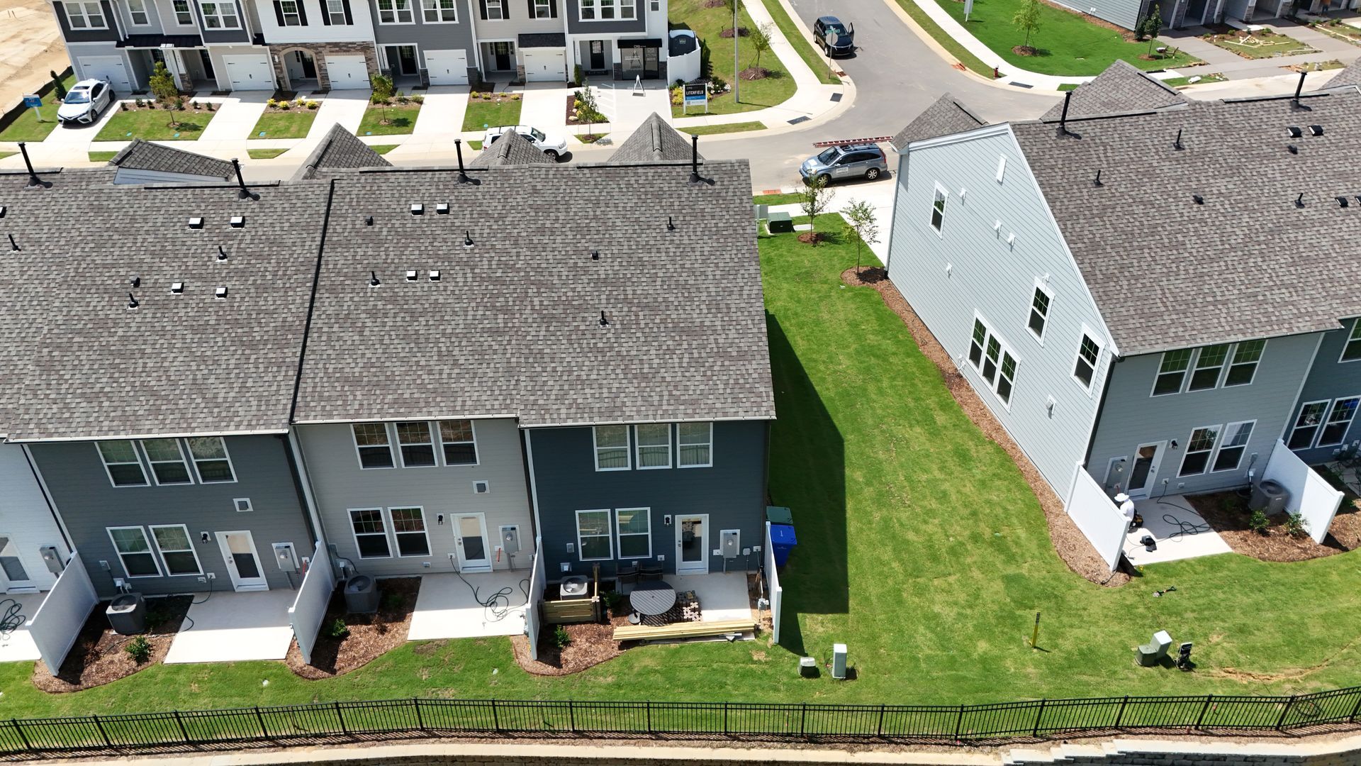 Aerial view of townhouses with gray roofs, green lawns, and a street.