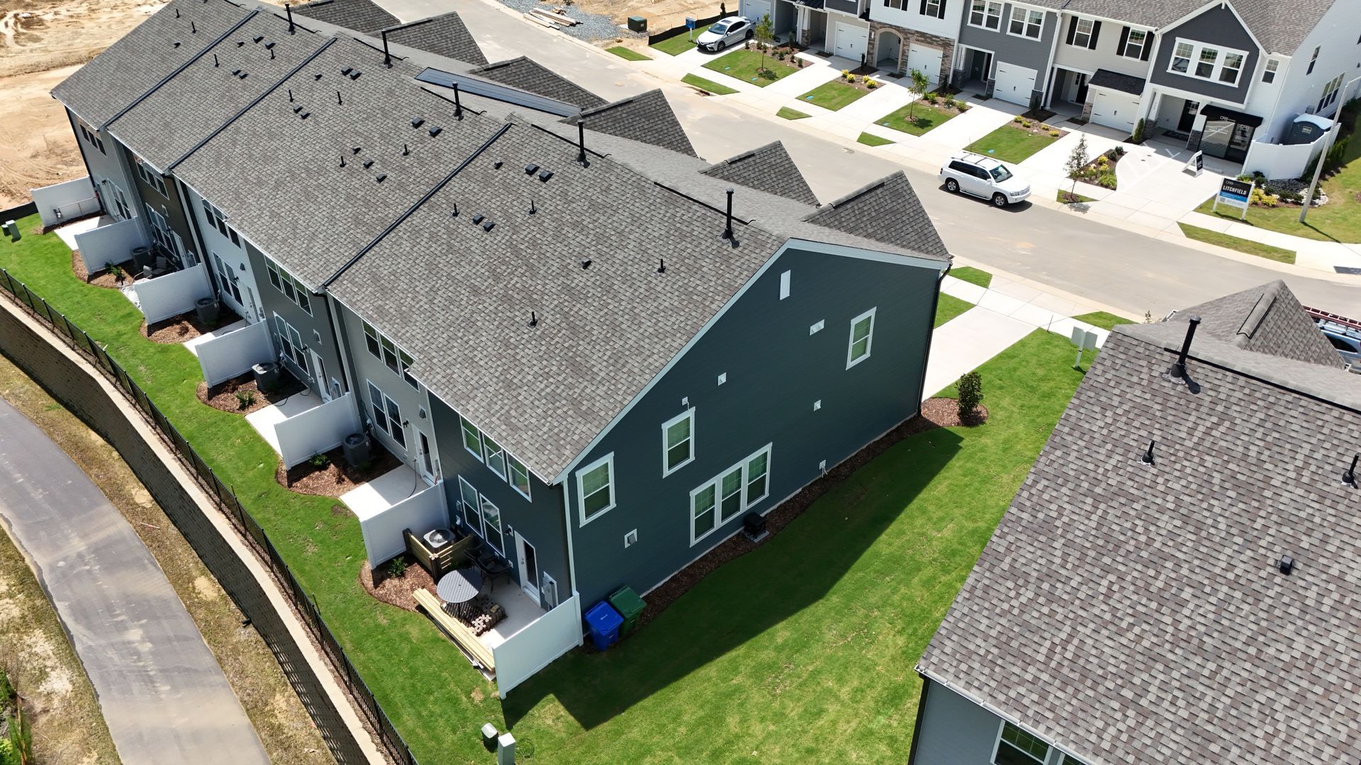 Row of modern townhouses with dark blue siding and gray roofs, green lawns.