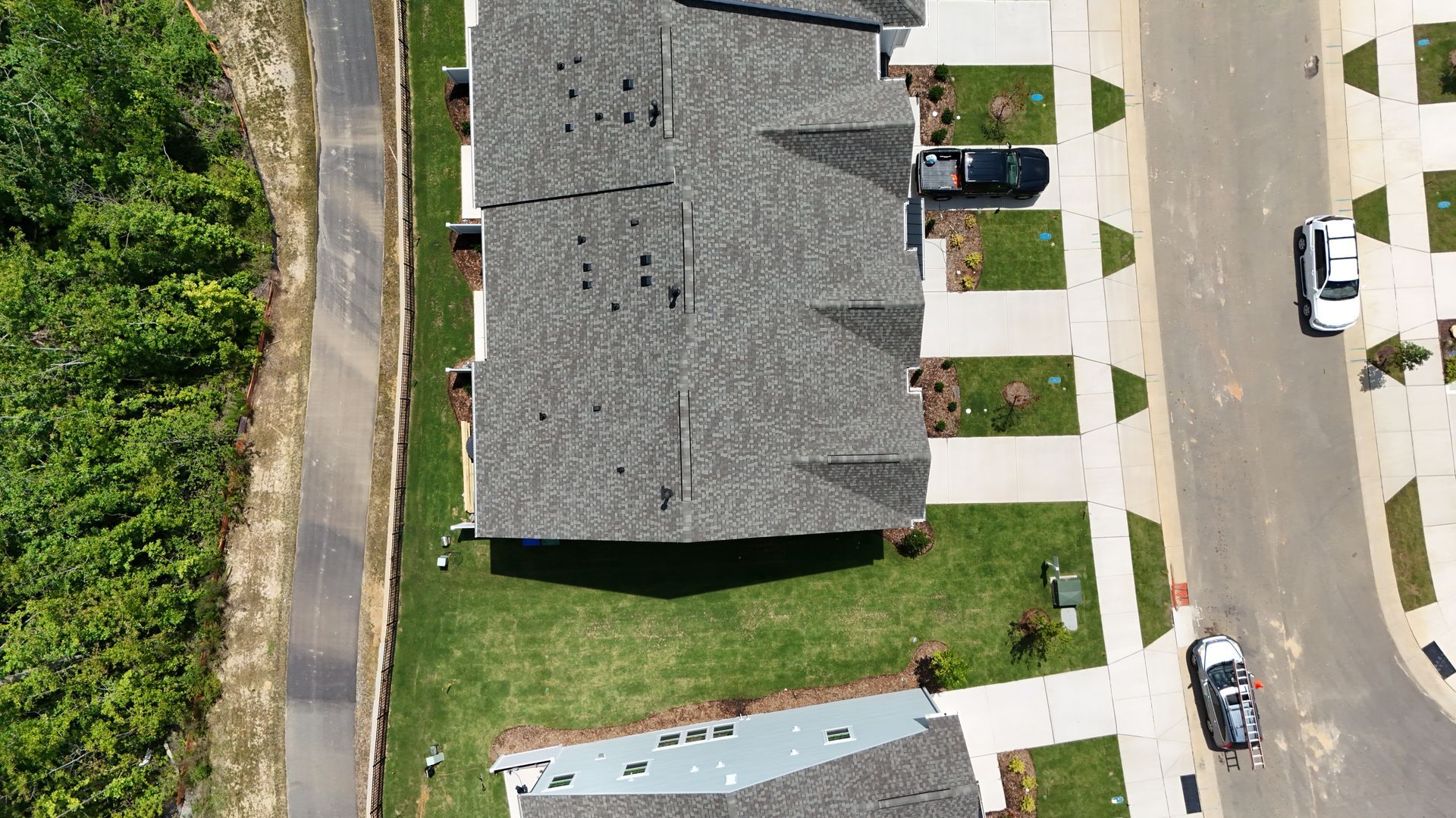 Aerial view of a row of houses with gray roofs, cars, green lawns, and roads.