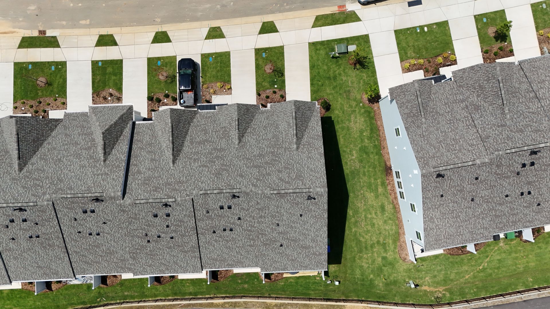Aerial view of gray-roofed townhouses with green lawns, sidewalks, and a street.