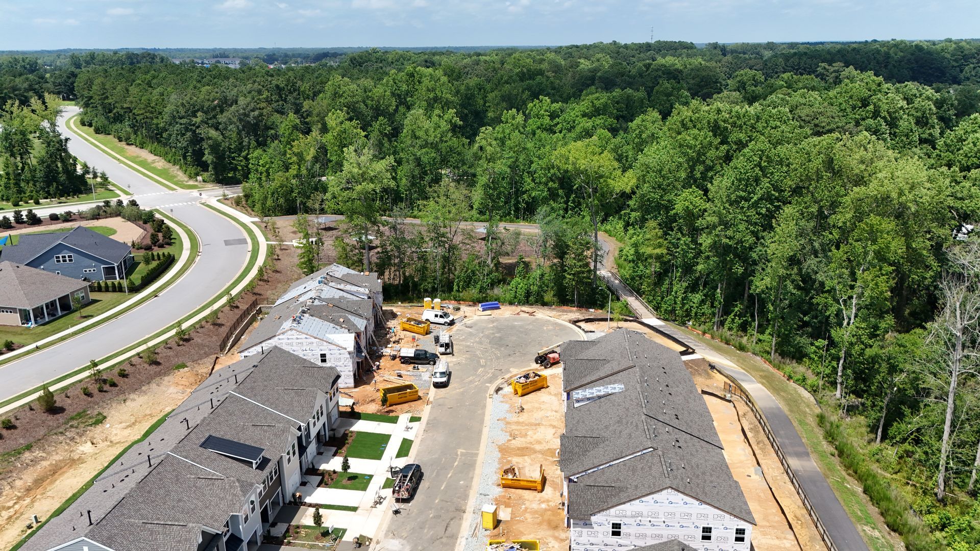 Aerial view of new townhouses under construction near a curving road and a forest.