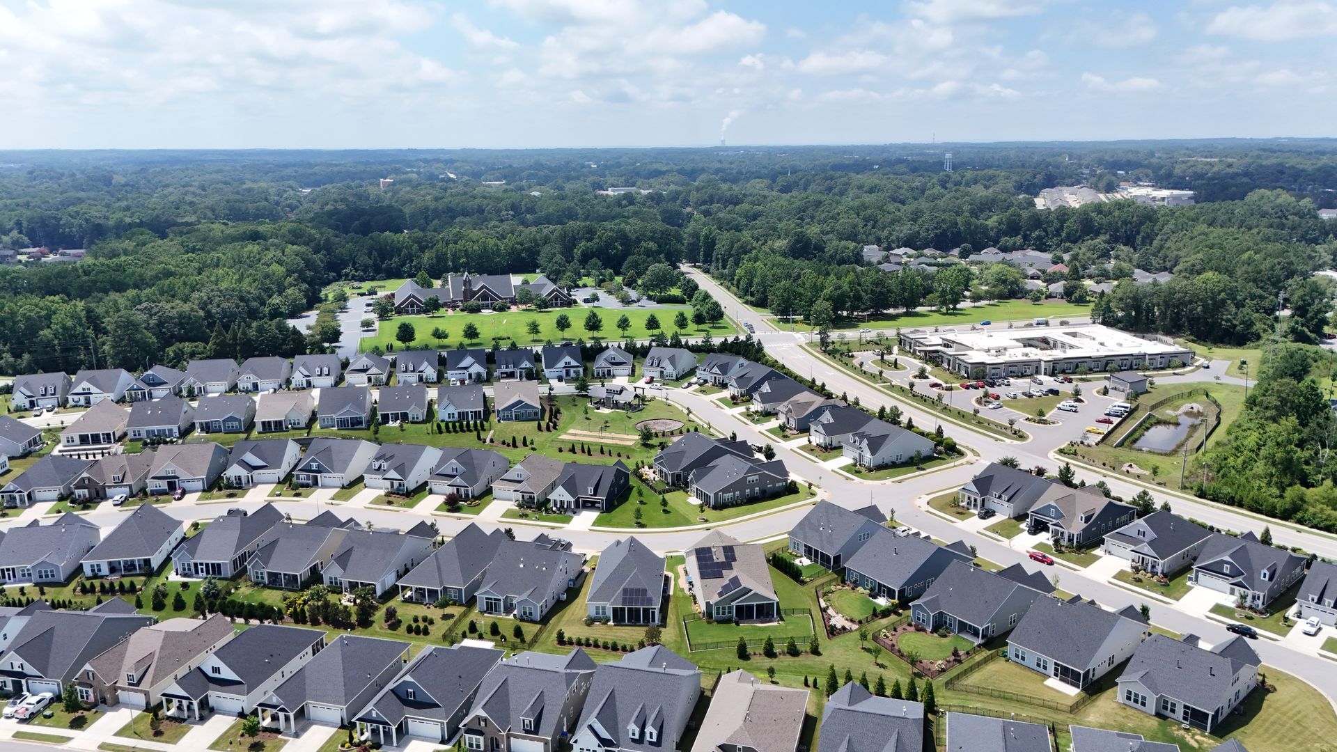 Aerial view of a suburban neighborhood with rows of houses, green lawns, and trees on a sunny day.