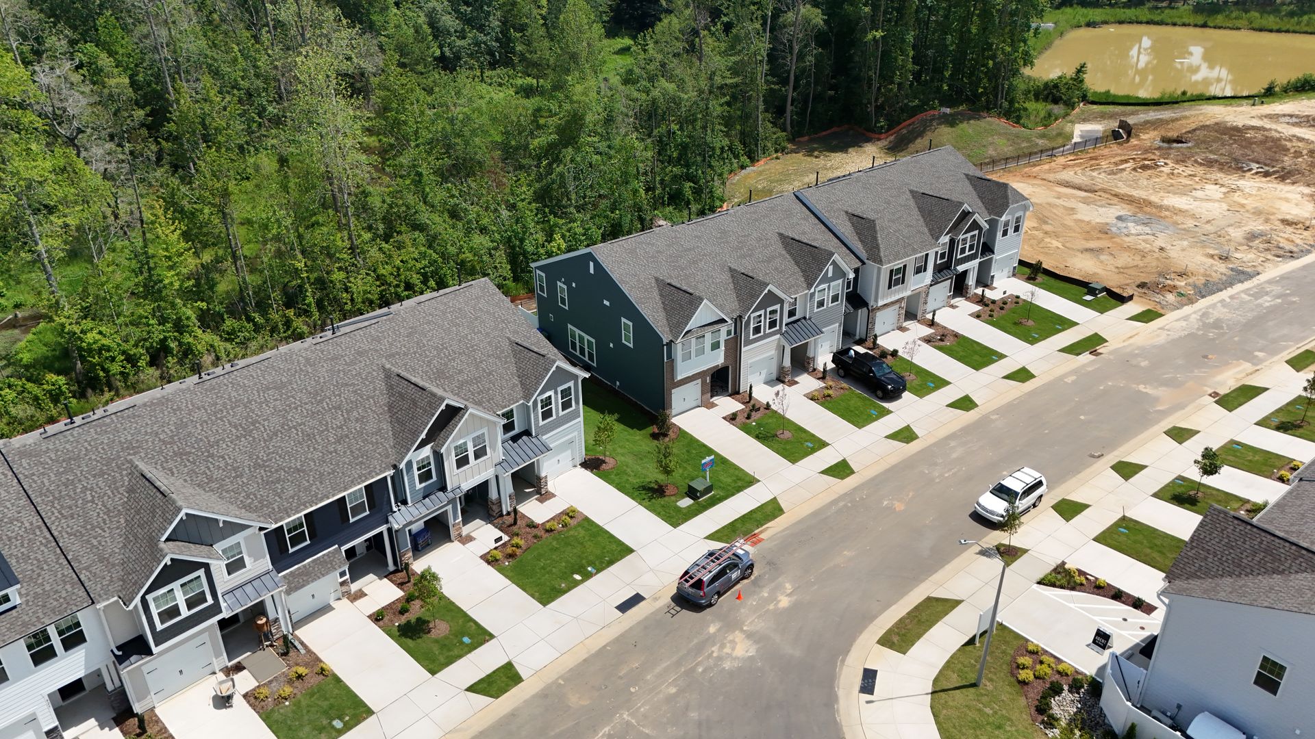 Rows of new townhouses in a suburban setting with cars on the street and a pond in the distance.