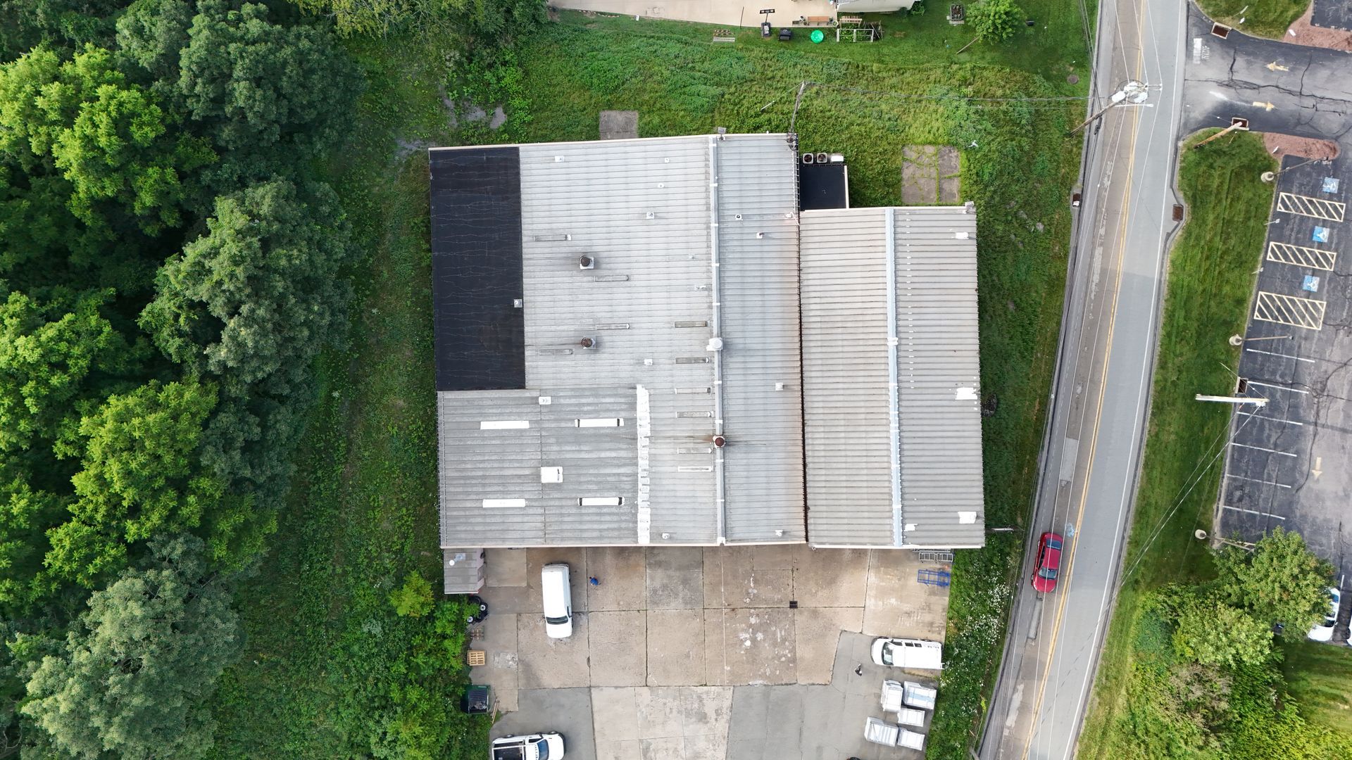Aerial view of a factory with multiple sections, a parking area, and road alongside green vegetation.