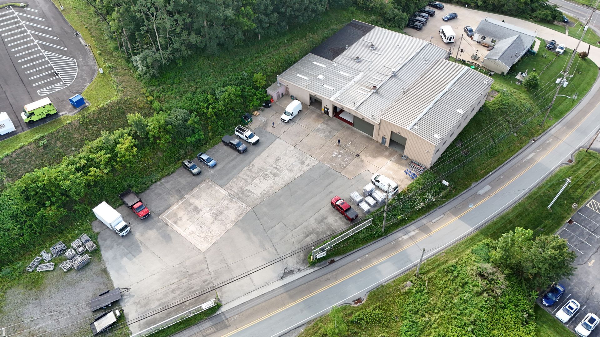 Aerial view of a building with a large paved area, vehicles, and a parking lot.