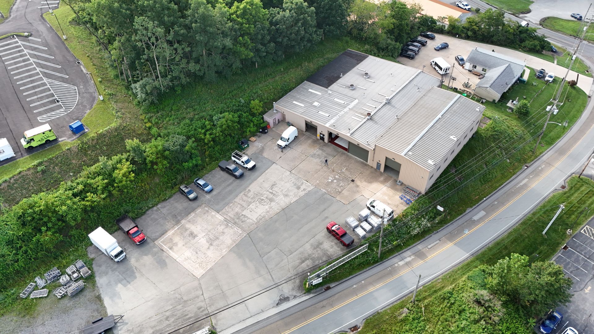 Aerial view of a car repair shop with parked vehicles. Green trees and a parking lot surround the building.