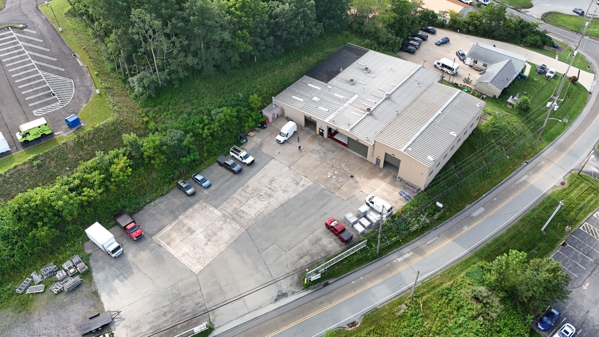 Aerial view: a building with vehicles parked outside, near a road and trees.