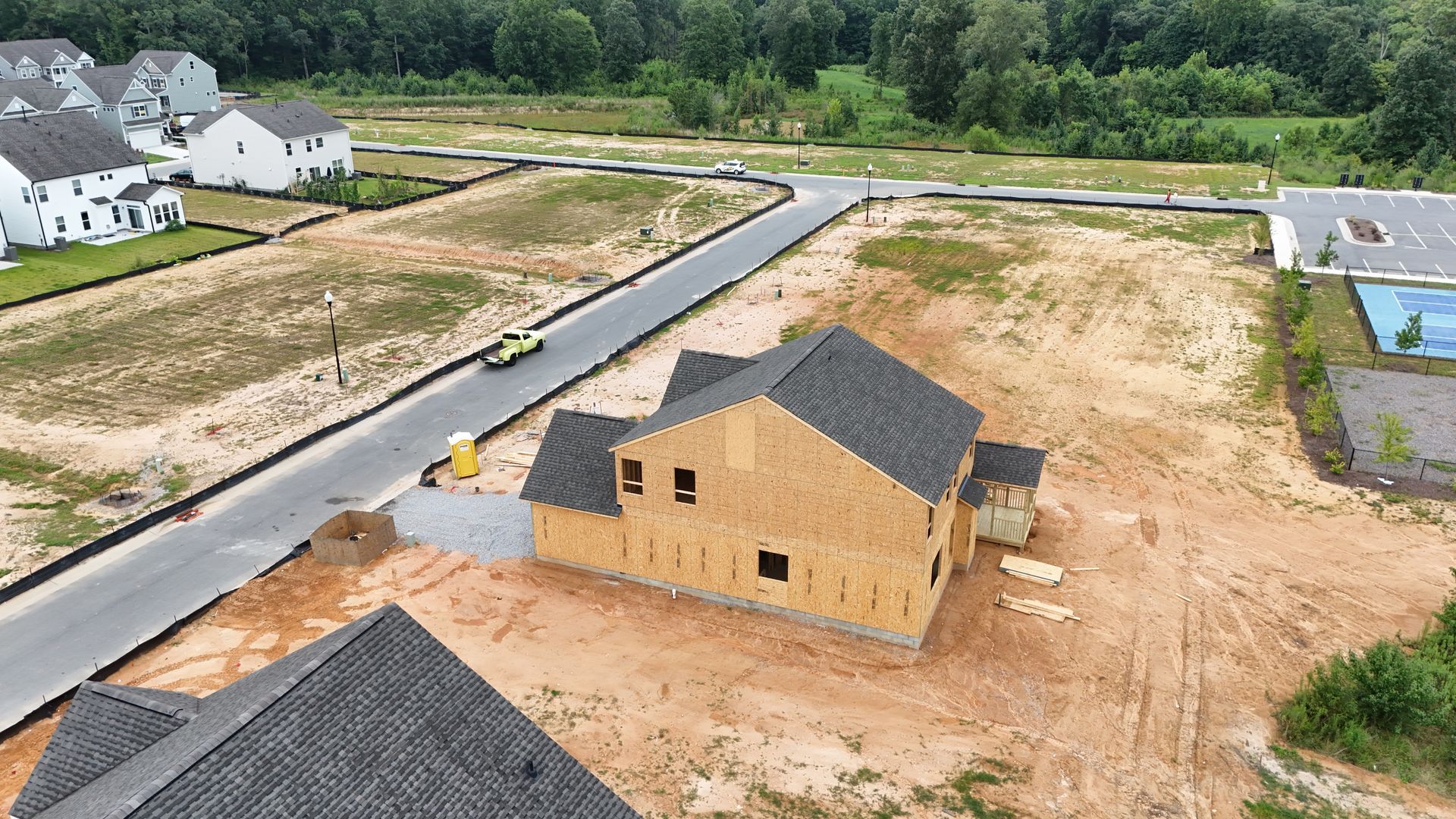 New houses under construction in a development; wooden frames, dirt, road, and completed homes visible.