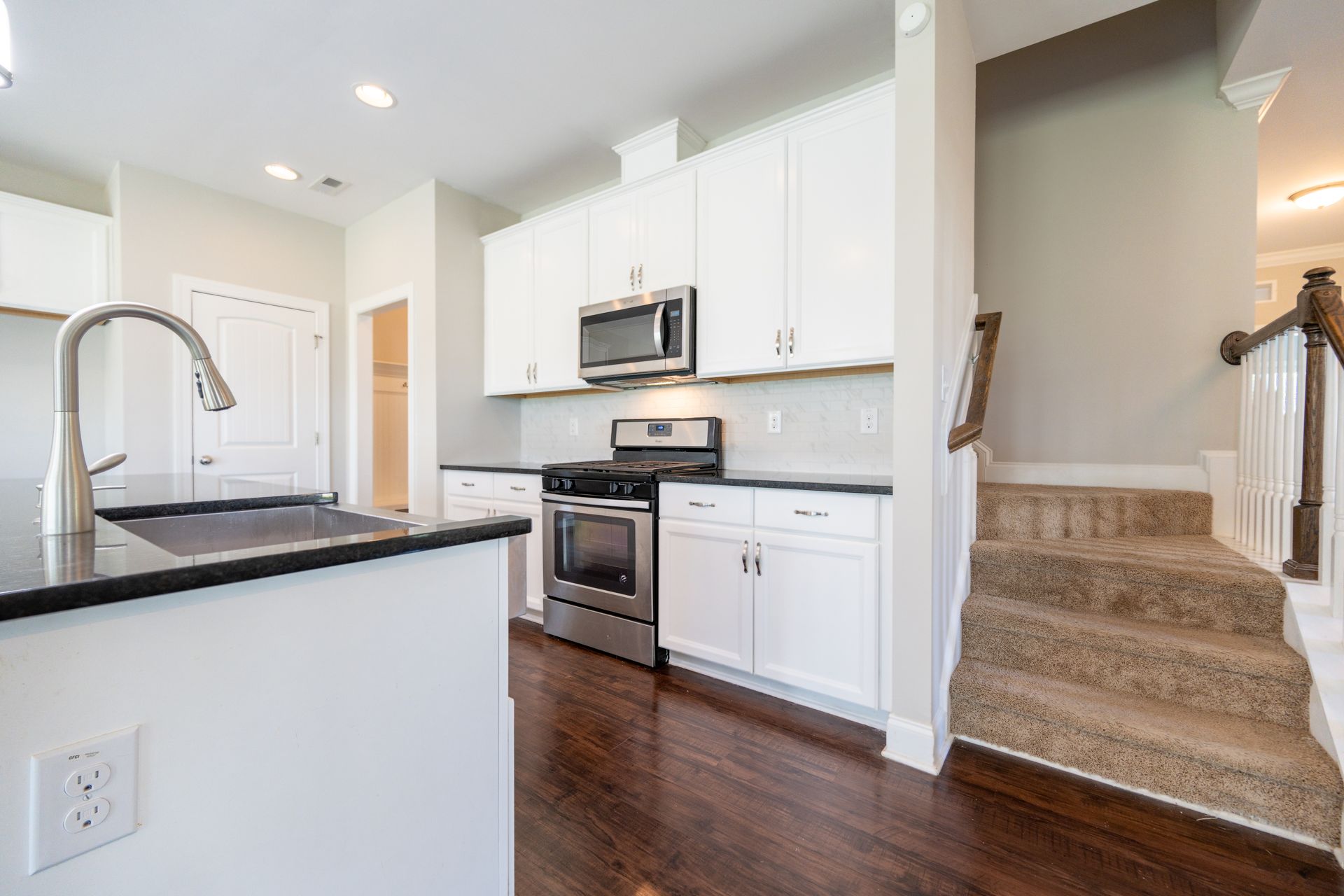 Modern kitchen with white cabinets, dark countertops, stainless steel appliances, and a staircase.