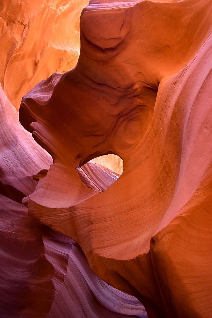 Smooth, swirling sandstone walls in shades of orange, red, and purple, creating a natural, otherworldly cavern.