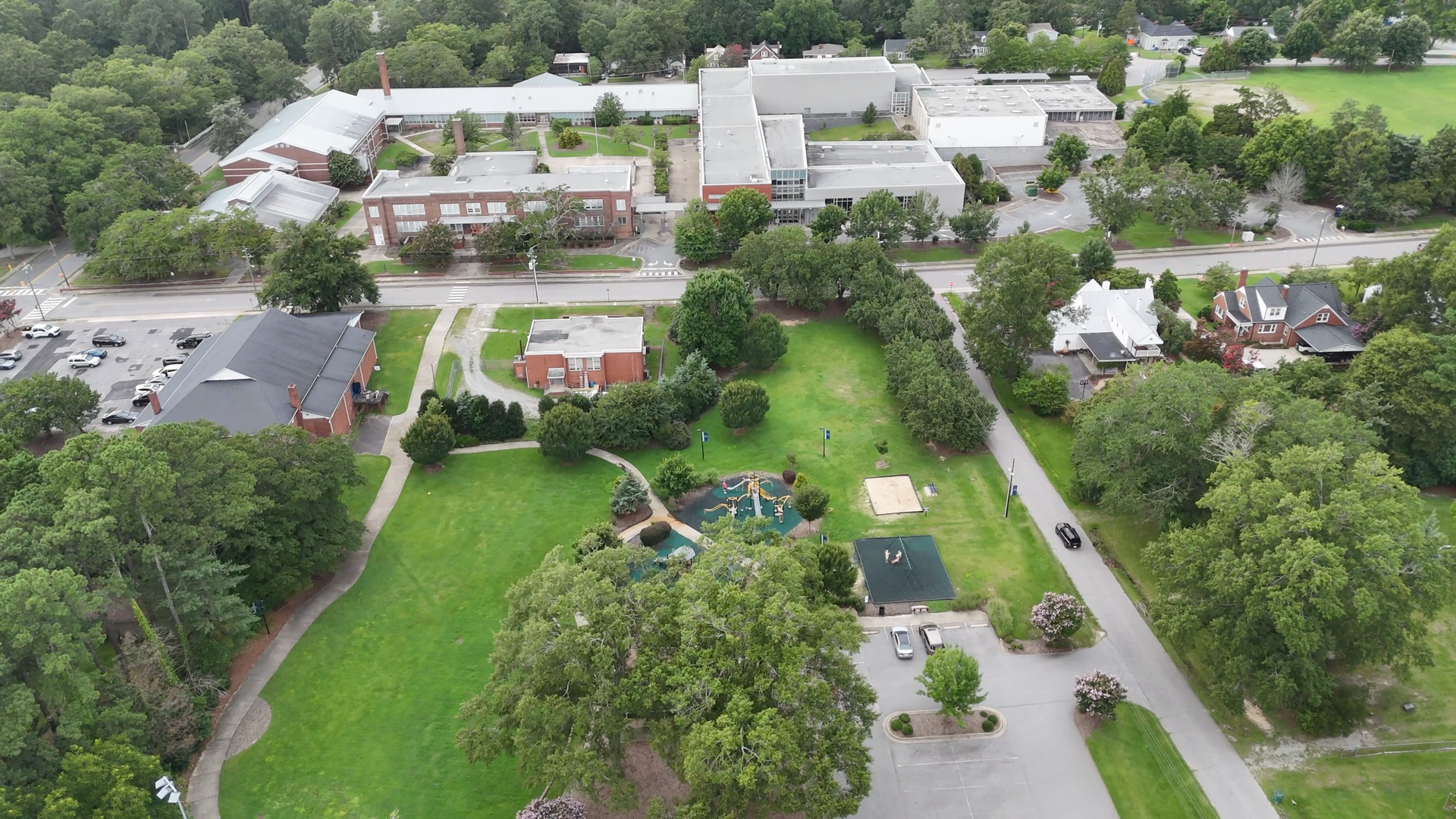 Aerial view of a school campus with buildings, playground, green space, and surrounding trees.