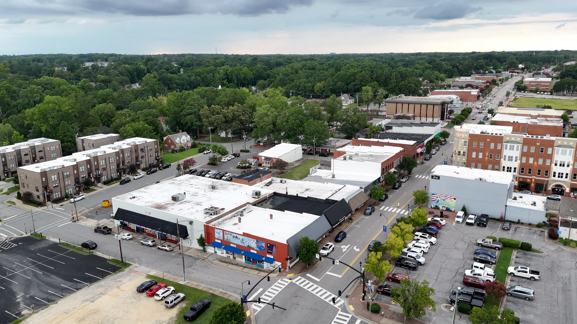 Aerial view of a small town's main street with shops, cars, trees, and a cloudy sky.