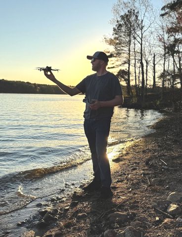 A man is holding a drone in front of a body of water
