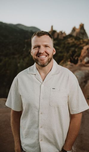 A man with a beard is wearing a white shirt and smiling.