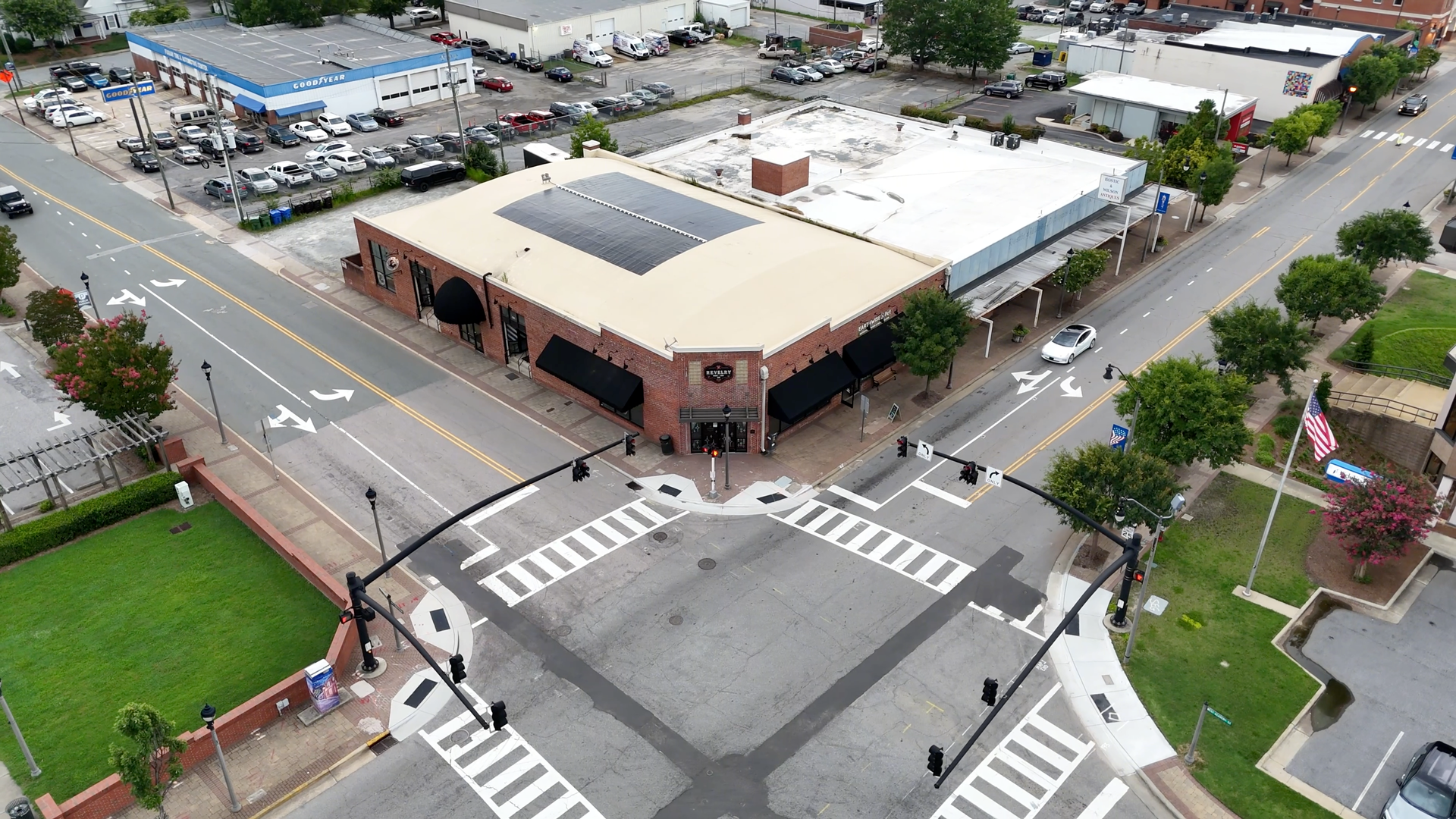 Aerial view of a multi-building intersection; brick and white buildings, crosswalks, and cars at the cross.