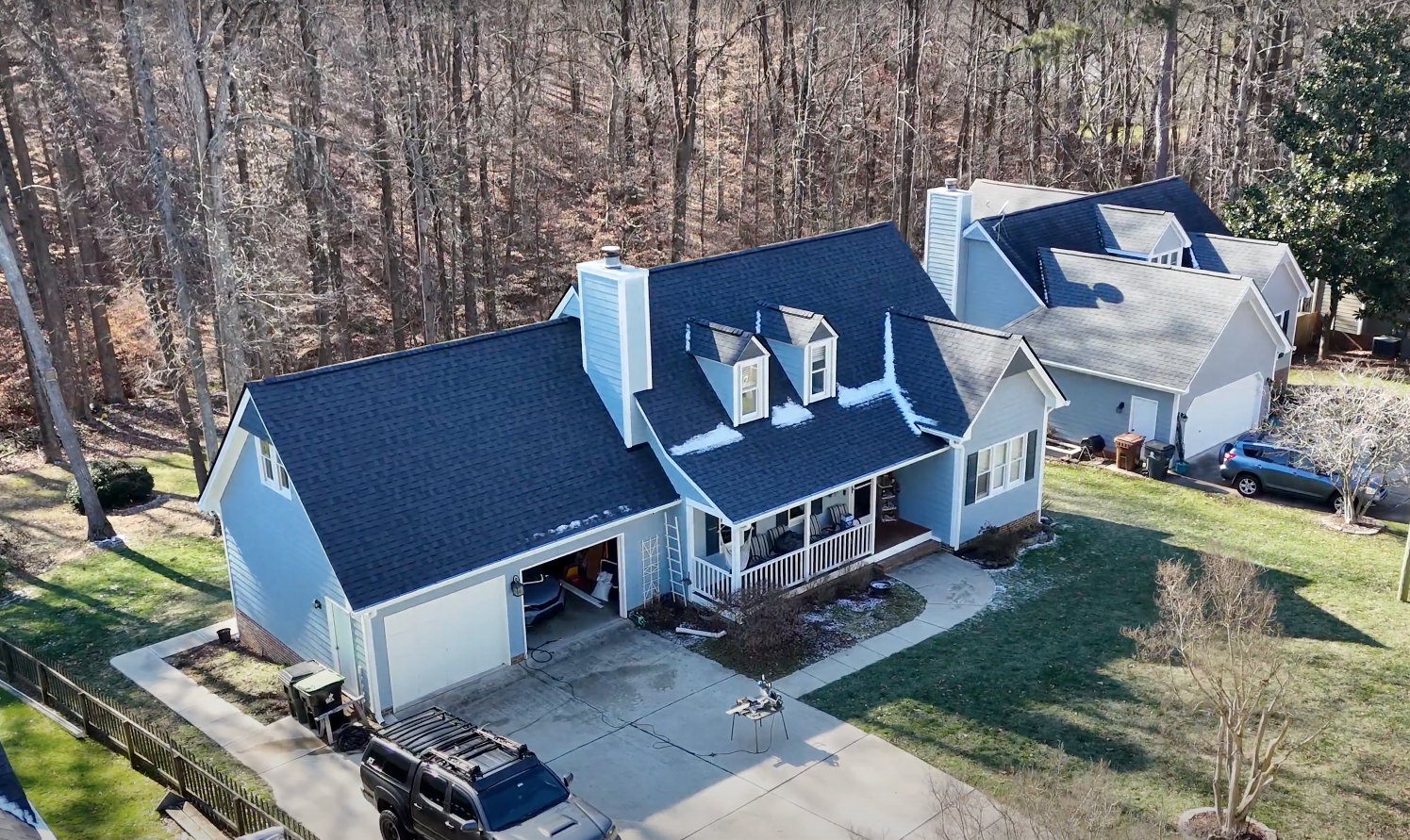 Blue house with dark gray roof, driveway, surrounded by trees.