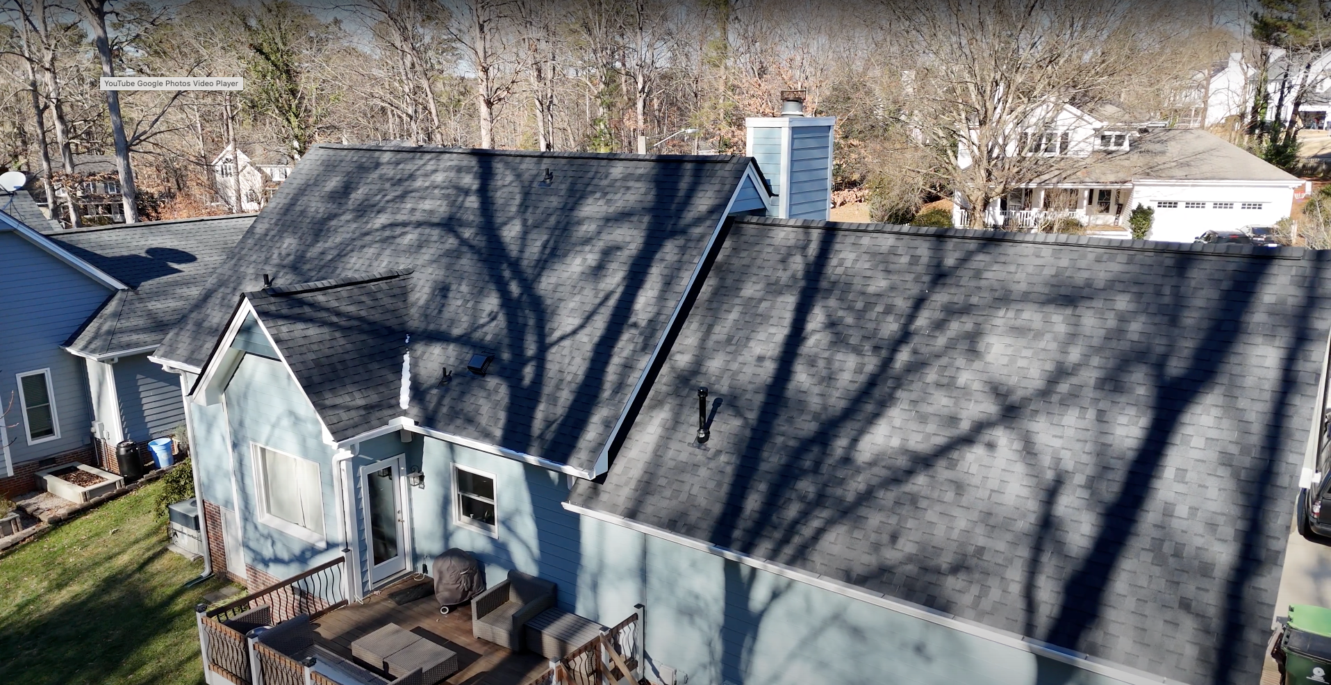 Blue house with dark roof and chimney, shadows of trees cast on roof.