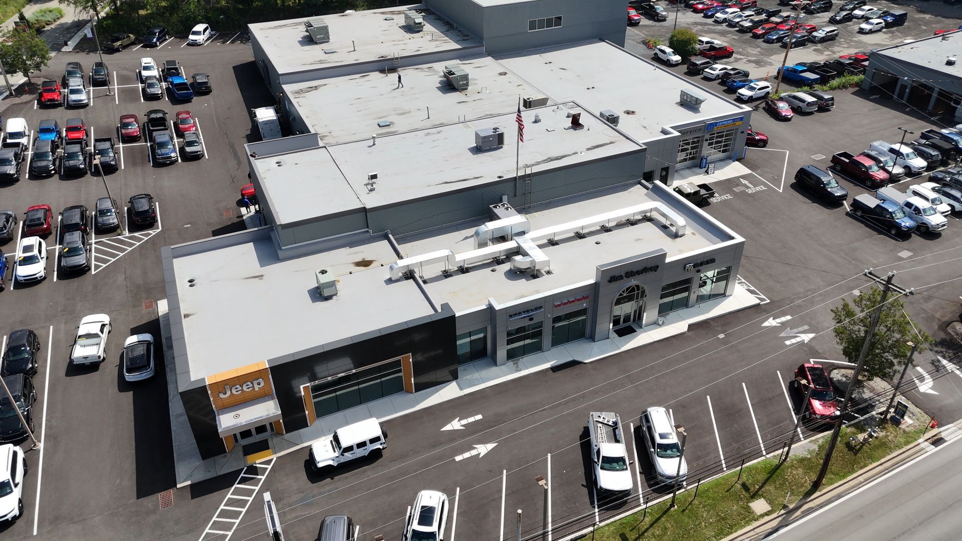 Aerial view of a Jeep dealership; rows of cars in parking lots, a large gray building with the Jeep logo.