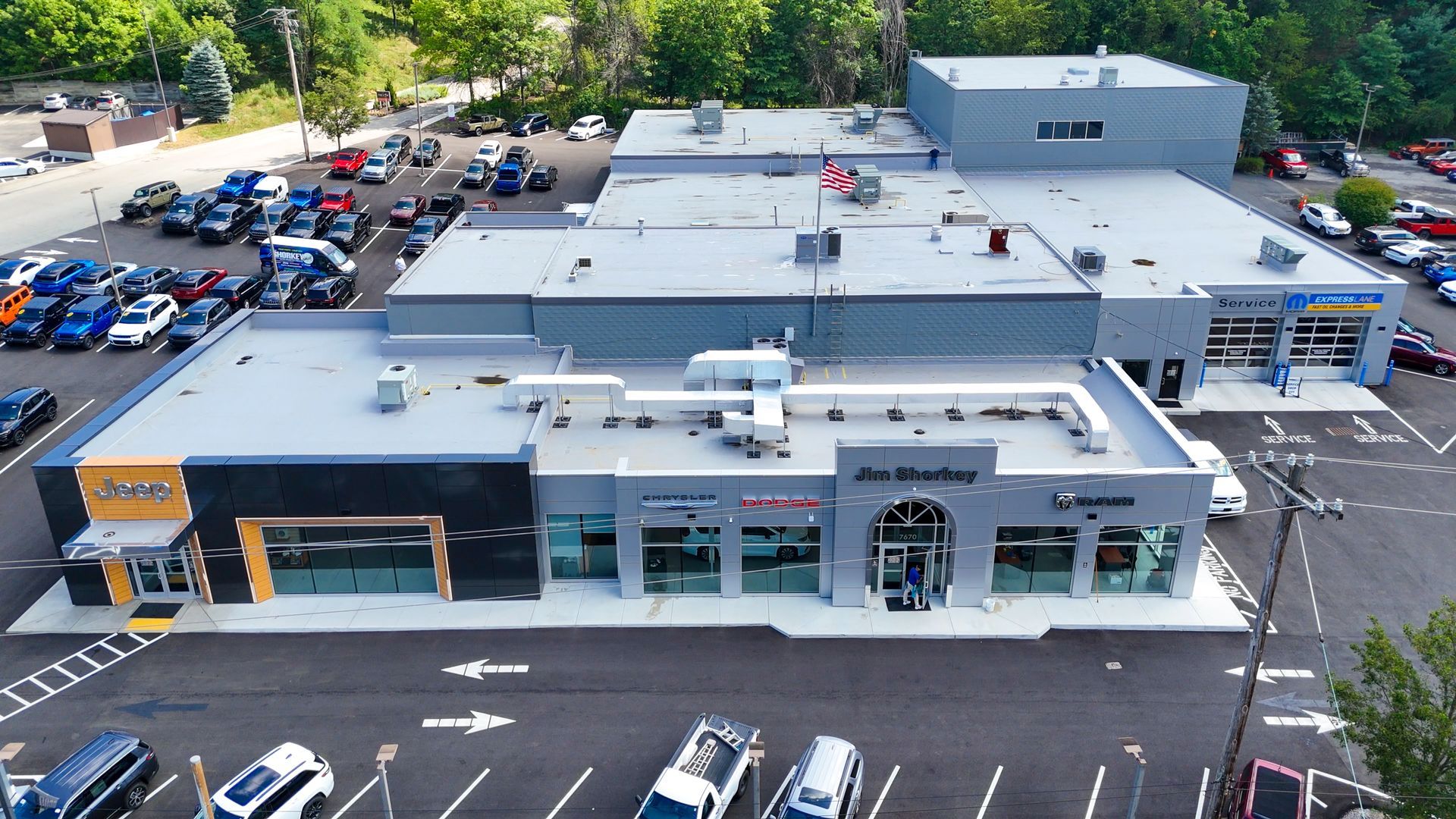 Aerial view of a car dealership with parked cars, buildings, and a few trees.