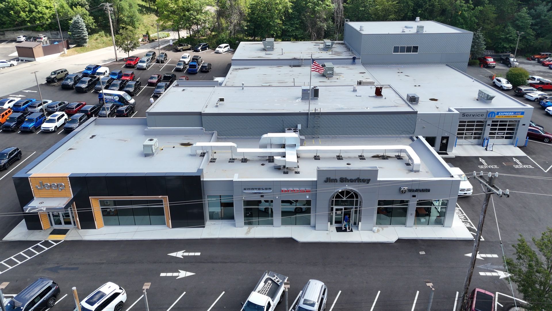 Aerial view of a car dealership with several buildings, parking lots, and numerous cars. Gray and blue colors dominate the scene.