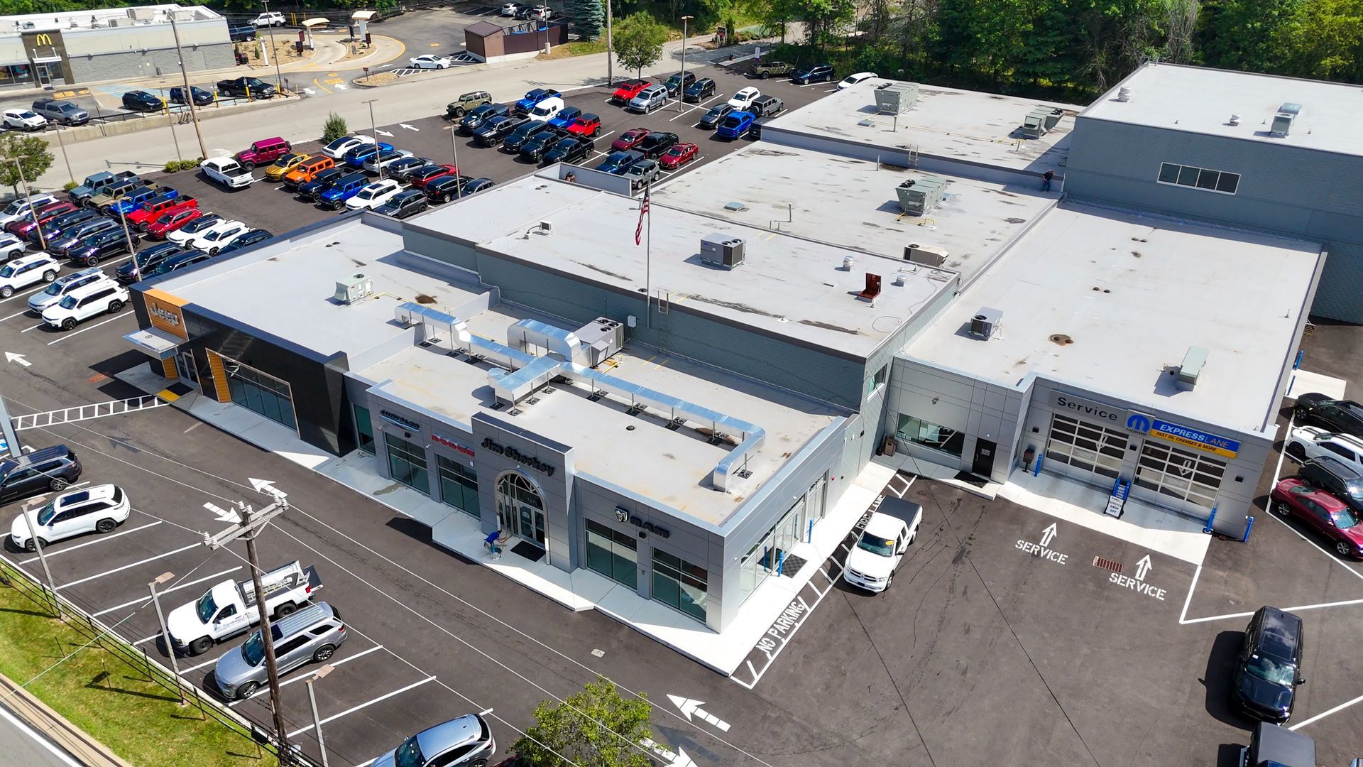 Aerial view of a car dealership with parked cars, a building with multiple bays, and a parking lot.