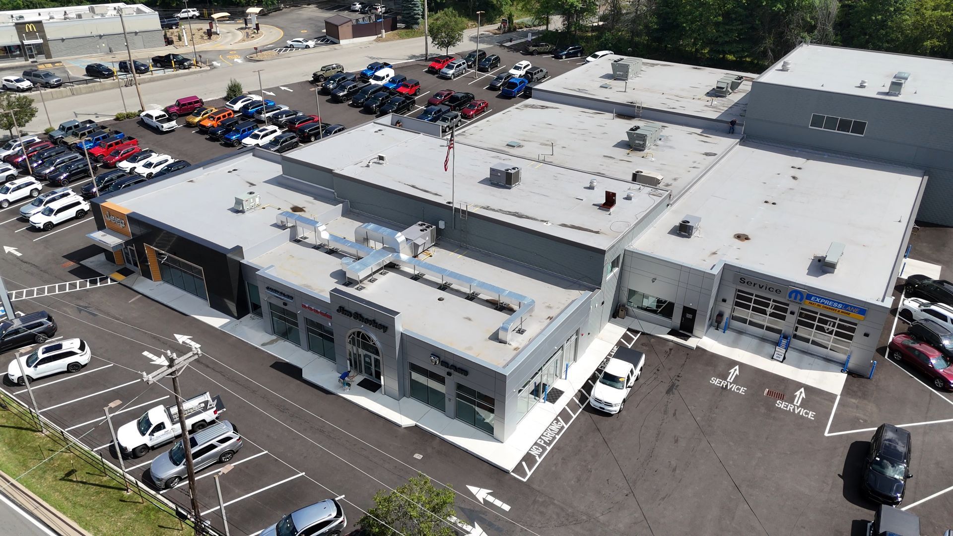 Aerial view of a car dealership with cars parked in front of a gray building on a sunny day.